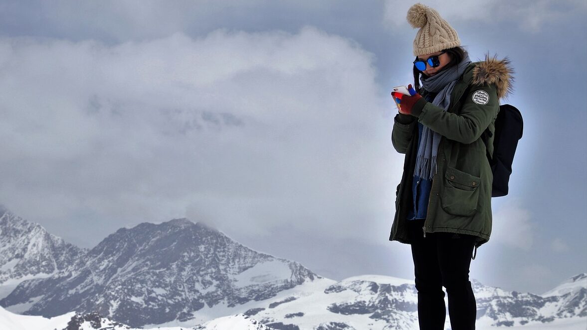 a woman on a snow covered mountain using her mobile phone depicting 24/7 customer service availability, around the world flights, RTW